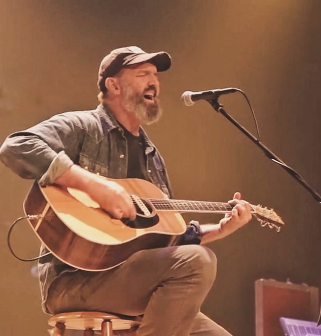 craig tanner playing guitar sitting in front of a microphone